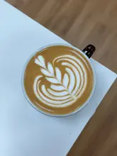 White ceramic cup of coffee with intricate latte art, surrounded by vibrant pink tulips.