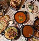 A top-down flat lay shot of a generous Indian feast at Dishoom Permit Room, featuring a variety of curries, naan, and sides arranged on a branded paper tablecloth.