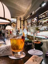 A sophisticated, atmospheric shot of two cocktails on a bar counter, capturing the upscale ambiance of a high-end hotel bar. The shallow depth of field effectively highlights the drinks while blurring the background, creating a professional and inviting aesthetic.