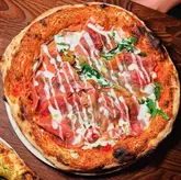 Gourmet La Crudo pizza at Marco's, London, with prosciutto, cherry tomatoes, rocket & parmesan fondue on a crispy base.