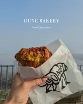 A close-up shot of a pastry held in a branded paper bag, set against a foggy, grey background in South Queensferry.