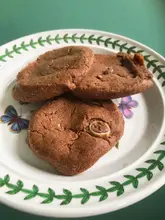 A casual, top-down photograph of three baked cookies served on a patterned plate, showcasing a store-bought cookie dough product.