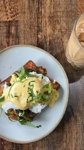 A promotional reel for Olive & Twist, featuring a creator introducing the venue as a cafe by day and cocktail bar by night. The video highlights the interior decor, specifically the twinkly lights and greenery, and showcases brunch dishes including a brisket baguette and eggs florentine on French toast. It also mentions the venue is dog-friendly.