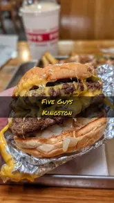 Classic Five Guys cheeseburger and a cup overflowing with golden fries, next to a box of peanuts on a table.