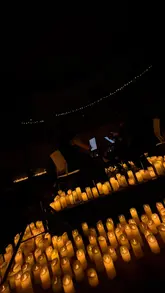 The video features a montage of a string quartet performing in a dimly lit room filled with numerous LED candles, creating an intimate and atmospheric experience. The footage focuses on the musicians and the ambient lighting, highlighting the aesthetic of the event.