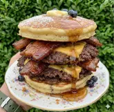 Pancakes, double-seared steak patties, maple-glazed bacon, Biscoff injection, gold leaf, and cookie crumbs stacked high.