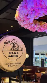Here are a few options for your alt text, kept under 125 characters:

**Option 1 (Descriptive):**
Platter of fresh sushi and ramen at Maki & Ramen restaurant with floral decor and a welcoming atmosphere.

**Option 2 (Action-oriented):**
A delicious spread of freshly made sushi and hot ramen served at Maki & Ramen in the Metrocentre.

**Option 3 (Concise):**
Freshly prepared sushi and ramen dishes served in the beautifully decorated Maki & Ramen restaurant.