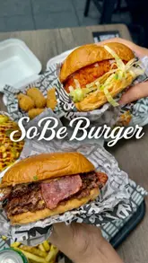 Here are a few options for your SEO alt text, keeping under the 125-character limit:

**Option 1 (Descriptive):**
Double Bacon Black Garlic burger, loaded cheese fries, and wings from SoBe Burger in Luton.

**Option 2 (Action-focused):**
A delicious spread of SoBe Burger meals, including a signature bacon burger, fries, and milkshakes in Luton.

**Option 3 (Keyword-rich):**
Best burgers and loaded fries at SoBe Burger near Luton train station, featuring their signature black garlic burger. 

**Recommendation:** Go with **Option 1 or 3** as they include both the brand name and the location, which are the most important elements for local SEO.