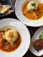 A high-quality, overhead food photography shot showcasing a lunch deal at Sepoy Club in Bath, featuring two distinct curry dishes with rice and a side of naan bread on a dark wooden table.
