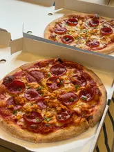 A top-down, casual shot of two pizzas in open cardboard takeaway boxes, likely taken at home or in a casual setting. The image captures the pizzas clearly but lacks professional styling or presentation.