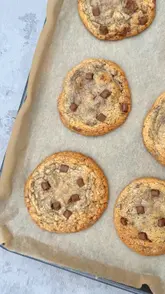 A short, satisfying video showing the process of making cookies, from mixing the dough with chocolate chips and candies to scooping them onto a baking tray and showing the final baked result.