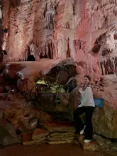 A photo of a visitor standing inside a large, illuminated cave at Cheddar Gorge, showcasing the natural rock formations and the tourist experience.