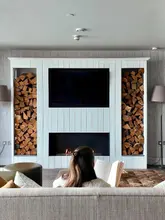 A high-quality, symmetrical shot of a person relaxing in a cozy hotel lounge, reading a book in front of a modern fireplace with wood storage. The image conveys a sense of luxury, comfort, and relaxation, typical of a high-end hotel stay.
