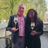 A photograph of two individuals posing with glasses of rosé wine on an outdoor balcony, likely at a promotional event for a winery.