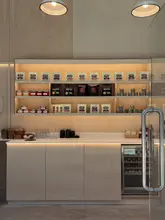 A clean, aesthetically pleasing, and well-lit photograph of a cafe's retail display shelves. The image showcases a variety of neatly arranged jars and bags of coffee or tea products against a minimalist plywood background, creating an inviting and professional atmosphere.