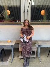 A lifestyle-focused portrait of a woman posing with a magazine outside a cafe, showcasing the venue's outdoor seating area.