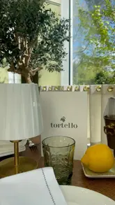 A montage showcasing a visit to Tortello restaurant, featuring shots of the interior, various Italian dishes like seafood pasta and tiramisu, cocktails, and a walk in the nearby park.