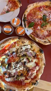 A short, engaging video showcasing a visit to Rudy's Pizza. The footage includes an exterior shot, a look at the open kitchen and pizza-making process, and close-ups of the food, including pizzas, olives, drinks, and dessert. The video captures the casual, authentic atmosphere of the venue.