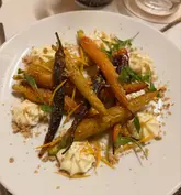 A top-down, well-composed shot of a roasted carrot dish featuring whipped feta and a crumble topping, served in a modern restaurant setting.