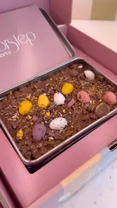 Here are a few options for your SEO alt text, keeping under the 125-character limit:

**Option 1 (Descriptive & SEO-focused):**
A person holding and eating a delicious Mini Egg and Kinder chocolate Crunch Cake from Doorstep Desserts in Leicester.

**Option 2 (Action-oriented):**
Close up of a warm, gooey chocolate Crunch Cake from Doorstep Desserts, featuring Mini Egg and Kinder toppings.

**Option 3 (Concise):**
Delicious chocolate Crunch Cakes with Mini Egg and Kinder toppings from Doorstep Desserts UK.

**Tip:** Option 1 is likely your best bet for SEO as it includes the location ("Leicester") and the brand name ("Doorstep Desserts").