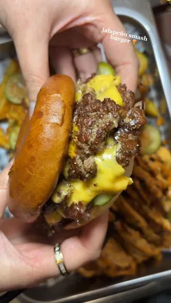Close-up of a smashburger from Dark Burg, featuring two patties, melted cheese, and fresh toppings, next to loaded fries.