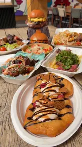 Here are a few options for your SEO alt text, depending on what the photo shows:

**Option 1 (Focus on the food - best for SEO):**
"A spread of gourmet burgers, pasta, and fried chicken from various street food vendors at Herbert's Yard."

**Option 2 (Focus on the atmosphere/location):**
"Happy customers enjoying a variety of street food dishes at the outdoor Herbert's Yard dining area."

**Option 3 (General/Descriptive):**
"A delicious feast of burgers, pasta, wings, and doughnuts from street food traders at Herbert's Yard."

**SEO Tip:** Since alt text is for accessibility and search engines, it's best to describe the **actual food or scene** in the photo rather than the caption text. Choose the one that most closely matches what is physically visible in your image.