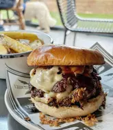 A close-up, appetizing shot of a loaded burger with brisket and cheese, served with a side of fries. The image captures the texture of the food well, though the composition is slightly cramped and the background includes a distracting element.