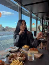 A lifestyle-focused shot featuring a woman enjoying a drink and a selection of small plates at a rooftop venue with a city skyline view.
