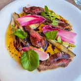 A high-quality, top-down photograph of a plated steak dish featuring seared beef, radicchio or chicory leaves, and watercress, served on a white plate.