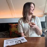 A lifestyle-focused shot of a woman smiling while holding a glass of wine at a table in an Italian restaurant. A branded newspaper is placed on the table, adding to the venue's branding.