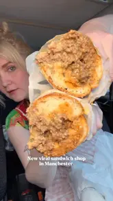 Manchester food blogger eating a messy, loaded sandwich, likely a beef or pastrami sandwich.