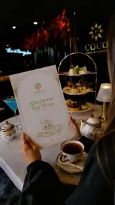 A montage video showcasing the 'Silk Route Afternoon Tea' at Coco Grill & Lounge in London. The video features shots of the venue's interior, the afternoon tea stand with various savoury and sweet items, tea service, and smoking cocktails, all set against a backdrop of Tower Bridge.