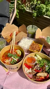 Here are a few options for your alt text, depending on the specific focus of the image:

**Option 1 (Focus on the food - best for SEO):**
Flat lay of various Pho restaurant gluten-free dishes including summer rolls and noodle bowls on a wooden table.

**Option 2 (Focus on the brand/campaign):**
Selection of Pho restaurant gluten-free meal bundles available on Deliveroo for Coeliac Awareness Month.

**Option 3 (Concise & descriptive):**
Close-up of fresh gluten-free Vietnamese food from Pho restaurant, featuring summer rolls and main noodle dishes.

**SEO Tip:** I recommend **Option 1**, as it uses descriptive keywords that search engines use to categorize the visual content of your image.