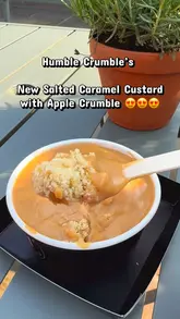 Here are a few options for your SEO alt text, keeping it under 125 characters:

*   **Option 1 (Descriptive):** Apple crumble with salted caramel custard and cold custard from Humble Crumble at Bicester Village.
*   **Option 2 (Action-oriented):** A delicious serving of Humble Crumble’s fan-favorite apple crumble topped with salted caramel and cold custard.
*   **Option 3 (Concise):** Close-up of a large apple crumble dessert with salted caramel and cold custard from Humble Crumble.