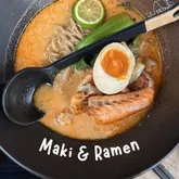 A high-quality, top-down photograph of a bowl of seafood ramen, featuring a perfectly cooked soft-boiled egg, bok choy, and a lime wedge. The lighting is bright and even, highlighting the textures of the broth and ingredients, with a clean, professional composition.