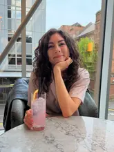 A high-quality, well-lit portrait of a woman enjoying a cocktail in a stylish venue with a view. The image captures a relaxed, social atmosphere suitable for a night out or drinks with friends.