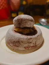 A close-up, eye-level shot of a dessert, identified in the caption as a brown butter and tonka bean madeleine with orange curd, served in a dimly lit wine bar environment.