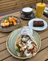 Here are a few options for your SEO alt text, depending on the specific image:

**Option 1 (Focus on the food - best for engagement):**
Delicious brunch dishes including a chicken shawarma flatbread and hot honey halloumi at Kofi & Co, Roundhay.

**Option 2 (Focus on the brand - best for local SEO):**
Customer enjoying a seasonal brunch, coffee, and smoothie at Kofi & Co cafe in Roundhay, Leeds.

**Option 3 (Concise & descriptive):**
A seasonal brunch spread with shawarma flatbread and halloumi bites at Kofi & Co restaurant in Roundhay.

**SEO Tip:** If the image shows the interior or the storefront, swap the food description for "The bright, airy interior of Kofi & Co cafe in Roundhay" to help Google understand the vibe of your content.