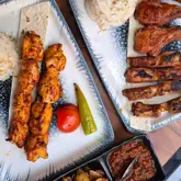 An overhead, flat-lay style photograph of a Turkish meal featuring plates of chicken shish and lamb chops served with rice, alongside a side dish of spicy dip.