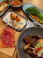 Here are a few options for your alt text, depending on what is most visible in your specific image:

**Option 1 (Focus on the food/spread):**
Delicious selection of tapas including beef short rib, chorizo, and monkfish skewers at El Gato Negro restaurant.

**Option 2 (Focus on the experience):**
Two people enjoying a variety of Spanish tapas dishes and a carafe of white sangria at El Gato Negro on Castle Street.

**Option 3 (Focus on the aesthetic/ambiance):**
Luxurious tapas spread with cocktails and sharing plates on a table at the newly refurbished El Gato Negro restaurant.

**SEO Tip:** If your image features a specific hero dish (like the beef short rib), make sure to mention that, as it is a high-intent search term for people looking for recommendations!