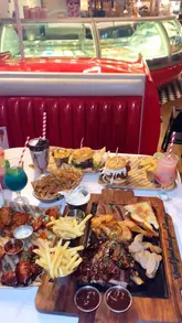Here are a few options for your SEO alt text, depending on what the image shows:

**Option 1 (Focus on the food - recommended):**
"Pitmaster Platter with brisket, lamb ribs, and Cajun chicken at Big Moe’s Diner, London Designer Outlet Wembley."

**Option 2 (Focus on the vibe):**
"Retro 50s-style American diner booth seating and neon decor inside Big Moe’s Diner at Wembley Park."

**Option 3 (General/Brand-focused):**
"Delicious American-style meat platter served at Big Moe’s Diner in London Designer Outlet, Wembley."

**SEO Tip:** The first option is generally the best for accessibility and search rankings because it describes both the specific meal and the location.