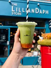 A bright, outdoor lifestyle shot featuring an iced matcha drink held in front of a local cafe storefront, capturing a summer vibe.