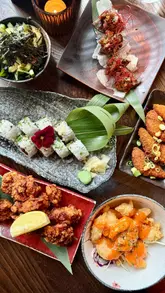 Here are a few options for your alt text, depending on the specific focus of the photo:

**Option 1 (Focus on the food - Recommended):**
"A delicious selection of Japanese small plates including Wagyu crispbreads and sushi at Kibou restaurant in Clifton."

**Option 2 (Focus on the experience):**
"Two people enjoying a variety of Japanese small plates and cocktails at Kibou restaurant in Bristol."

**Option 3 (Detailed/Descriptive):**
"Close-up of assorted Japanese dishes, including sushi, scallops, and croquettes, served at Kibou restaurant in Clifton."

**SEO Tip:** I’ve included the restaurant name, location, and key food terms ("Japanese small plates," "sushi") as these are the keywords people are most likely to search for when looking for food in Bristol.