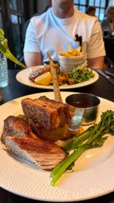 A montage video showcasing a riverside pub and restaurant, highlighting the outdoor seating area, interior dining space, and a selection of dishes including pate, chicken, and dessert.