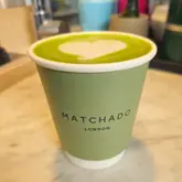 A close-up, eye-level shot of a matcha latte in a branded paper cup, featuring latte art, placed on a marble surface.
