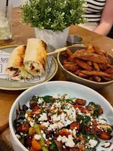 A high-angle, flat-lay style shot of a brunch spread featuring a wrap, a bowl of fries, and a halloumi salad bowl, taken at a cafe.