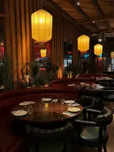 An atmospheric, wide-angle shot of a restaurant interior featuring warm, hanging lantern lighting and red leather booth seating. The image effectively communicates the mood and aesthetic of the venue, positioning it as a sophisticated space suitable for evening dining.
