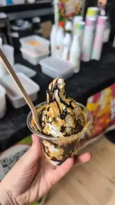 A montage video showcasing various food items purchased at a vegan fair, including sweets, pastries, dried fruits, baked goods, a sundae, and a plant-based meal of battered sausage and chips.