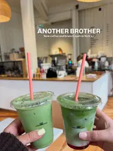 A first-person perspective shot of two iced matcha lattes held up in front of a cafe interior, promoting a new brunch spot in York.