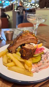 A promotional video for Bear Bones BBQ Co. at The Ghost at the Feast in Chichester, featuring close-up shots of various BBQ dishes including ribs, brisket, turkey, and mac and cheese, alongside glimpses of the venue's interior.